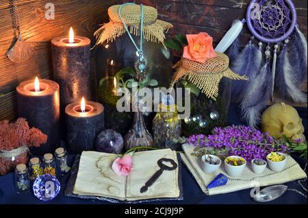 Stillleben mit offenem Tagebuch, Blumen, Flaschen mit Pflanzen und Zauberobjekten auf Hexentisch. Esoterischer, gotischer und okkulter Hintergrund, Halloween Mystic Co Stockfoto