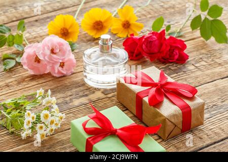 Geschenkschachteln mit Bändern und dem Parfüm auf den alten Holzbrettern mit den Blumen geschmückt verpackt. Draufsicht. Stockfoto
