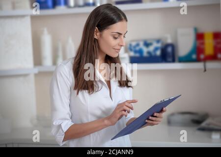 Bei der Arbeit. Kosmetikerin in einem weißen Gewand, die beschäftigt aussagend Stockfoto