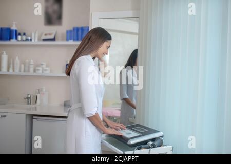 Machen Sie sich fertig. Kosmetikerin steht in der Nähe des Aparatus und drückt Knöpfe Stockfoto