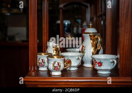 Alte Tee- und Kaffeetassen in einem Set mit Teekanne und Zuckerdose stehen im Café auf dem Regal. Inneneinrichtung Stockfoto