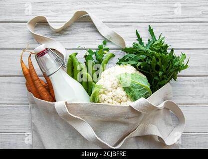 Frisches Gemüse in Öko-Baumwolltüten auf dem Tisch in der Küche. Karotte, grüne Erbsen, Kohl, Milch und Rucola vom Markt. Zero Waste Shopping-Konzept Stockfoto
