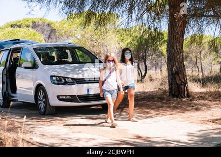 Mädchen springt mit einem Gesicht aus der Autotür Maske und helle Sonnenbrille glücklich mit ihren Armen offen für Nachdem wir die Sommerferien afte genießen konnten Stockfoto