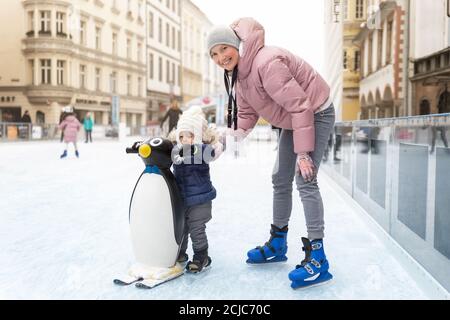 Junge Erwachsene attraktive schöne kaukasische Frau genießen Spaß mit kleinen Kleinkind Sohn im Freien Eisbahn während der Reise in der alten europäischen Stadt in Stockfoto