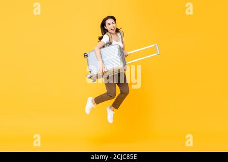 Aufgeregter, schöner Asian Tourist mit Gepäckspringen im Mittelluftstudio, der isoliert auf gelbem Hintergrund gedreht wurde Stockfoto