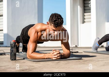 Muskulöser Sportmann, der Plank-Übung im Freien macht Auf dem Dach des Gebäudes Stockfoto