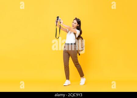 Junge hübsche asiatische Tourist Mädchen unter Selfie mit Digitalkamera In gelbem isoliertem Hintergrund Stockfoto