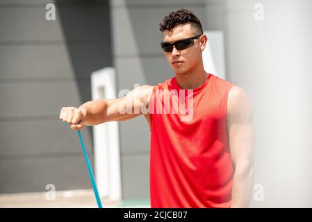 Handsome Sport Mann tun Schulter vorne erhöhen Übung mit elastischen Widerstandsband im Freien - Home Open Air Workout Konzept Stockfoto