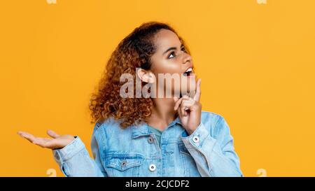 Seitenansicht Porträt der denkenden jungen afroamerikanischen Frau suchen Up tun offene Handfläche Geste in isolierten Studio gelben Hintergrund