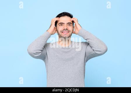 Überrascht stattlichen kaukasischen Mann schauen nach oben hält seinen Kopf mit Beide Hände isoliert in hellblauem Studiohintergrund Stockfoto