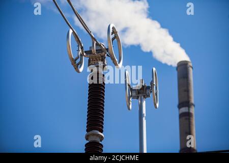 Kraftwerksanlage. Transformatorunterstation Hochspannungsausrüstung. Auf verschwommenem Fabrikschornstein mit weißem Rauch und blauem Himmel Hintergrund. Stockfoto