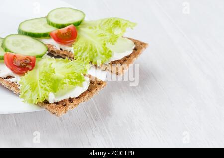 Frischer Sommer gesunde Vorspeise aus Vollkorn Roggen Chips Brot mit Gemüse - grüner Salat, Gurke, Tomaten, Frischkäse auf weißem Holzbrett, Klo Stockfoto