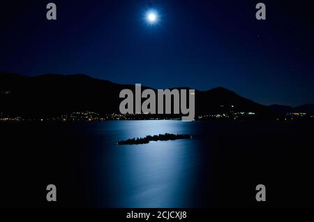 Mond Lichtreflexion über einem alpinen Lago Maggiore mit Brissago Inseln und Berg bei Nacht im Tessin, Schweiz. Stockfoto