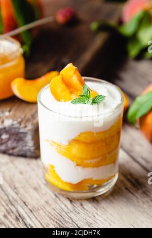 Pfirsichfrucht Dessert in Glas Tasse auf Holztisch. Hausgemachtes Dessert mit Früchten. Obstsalat mit Joghurt oder Sauerrahm. Stockfoto
