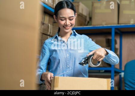 Portrait von Lagerarbeiter Frau Verpackung Karton mit klebrigen Band mit indischen Arbeiter Mann in lokalen Lager oder Fabrik, Industrie Und Exportbus Stockfoto