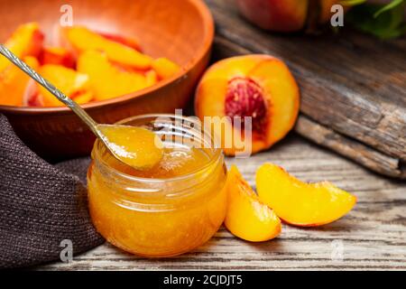 Peach jam in glass jar with peach wedges and whole peach fruit. Peach jam on wooden table Stock Photo