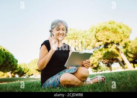 Ältere Frau chattet online mit seinem Tablet in einem Park Stockfoto