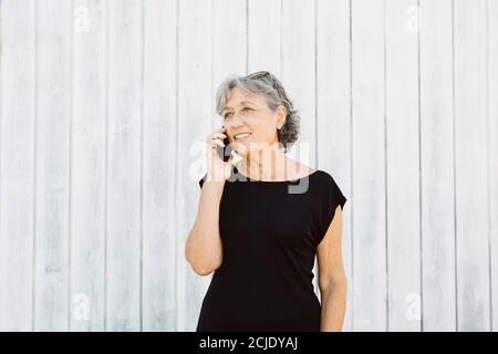 Ältere Frau, die über einem weißen Holz telefoniert Hintergrunde Stockfoto