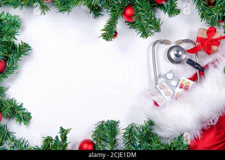 Medizinisches Banner mit Pillen, Geschenkschachtel, Stethoskop und Weihnachtsbaum auf weißem Holzhintergrund. Copyspace. Medizin im neuen Jahr flach Stockfoto