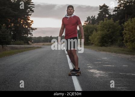 Ein Mann in einem roten T-Shirt reitet auf einem Skateboard auf der Autobahn, Stockfoto