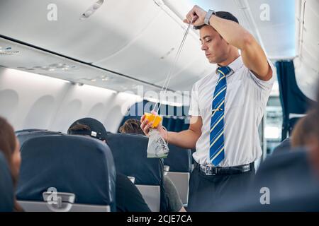 Mann mit Sauerstoffmaske, der die Sicherheitsverfahren vor dem Beifahrer vorführt Flugflug Stockfoto