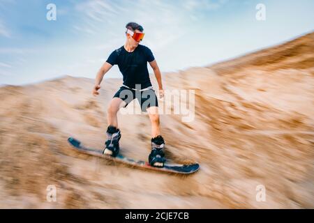 Extremer Absand auf Snowboard in der Wüste. Männlicher Snowboarder auf Dünen Stockfoto