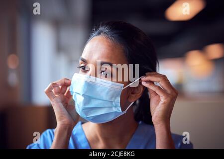 Weibliche Arzt In Scrubs Setzen Auf Gesichtsmaske Unter Druck Im Krankenhaus Während Der Gesundheitspandemie Stockfoto