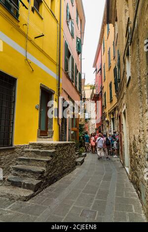 Touristen, die durch die schmale Hauptstraße Via Fieschi mit bunten Häusern auf jeder Seite im alten Dorf Corniglia an der Küste von... Stockfoto