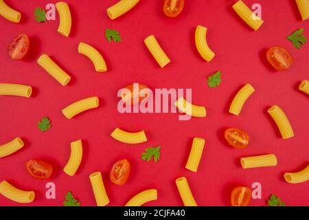 Macaroni, Tomaten und Petersilie Muster auf rotem Hintergrund. Italienisches Essen. Nudelzusammensetzung. Flaches Lay-Layout. Stockfoto