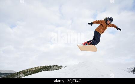 Konzept der extremen Arten von Sport. Snowboarder in farbenfroher Kleidung, die mit dem Snowboard gegen den bewölkten Himmel hoch fliegt. Low-Angle-Ansicht, Kopierbereich. Liebe zum Sport Stockfoto