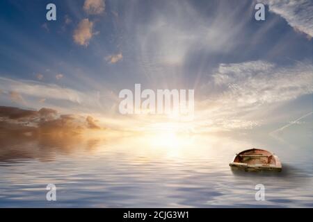 Verloren auf dem Meer, altes Ruderboot, das auf dem Meer in einem ruhigen Sonnenuntergang mit ruhigem Meerwasser herumbobbt. Kein Land nur Seestück und schöne Wolken. Stockfoto