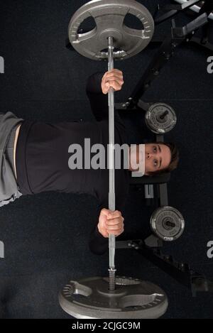 Draufsicht auf einen jungen, fitterten Mann, der eine Langhantel macht Bankdrücken im Fitnessstudio Stockfoto