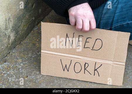 Arbeitsloser Mann sitzt auf dem Boden mit einem Schild aus Pappe, das sagt, dass Arbeit nötig ist Stockfoto