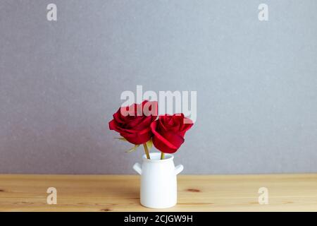 Rote Rosenblumen in Vase auf Holztisch mit grauem Hintergrund. Blumenarrangement, Kopierraum Stockfoto