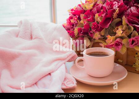 Rosa Tasse schwarzen Kaffee und die rosa floralen, über Holz Textur und Meereslandschaft Hintergrund. Entspannend und Kaffee-Konzept. Internationaler Kaffeetag Stockfoto