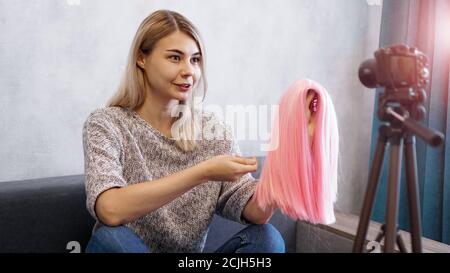 Bloggerin zeichnet Video auf. Sie spricht über Haarschnitte und zeigt eine rosa Perücke. Stylistin und Modeberater, die den Vortrag aufzeichnen Stockfoto