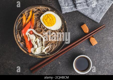 Asiatische Nudelsuppe mit Soba-Nudeln, Gemüse und Ei in Schüssel auf schwarzem Tisch. Draufsicht. Stockfoto