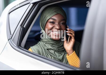 Schwarze muslimische Frau, die auf dem Rücksitz des Autos unterwegs ist und spricht Auf dem Handy Stockfoto