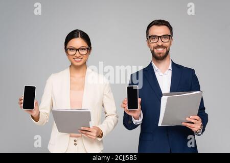 Paar interracial Kollegen halten Ordner und Smartphones mit Leerer Bildschirm isoliert auf grau Stockfoto