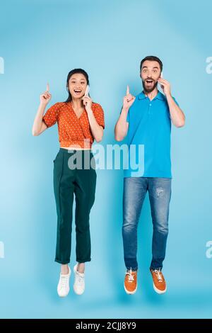 Aufgeregt interracial paar reden auf Smartphones und zeigen Idee Zeichen Während Sie auf Blau schweben Stockfoto