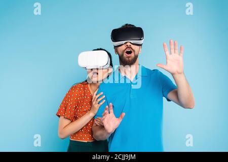 Verängstigte Frau in roten Bluse berühren aufgeregt Mann in Polo t-Shirt bei gleichzeitiger Verwendung von vr-Headsets isoliert auf blau Stockfoto