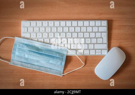 Chirurgische Maske neben Tastatur und Computermaus. Konzept der Covid-Pandemie und -Arbeit. Stockfoto