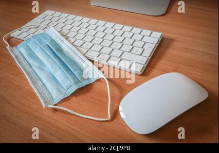 Chirurgische Maske neben Tastatur und Computermaus. Konzept der Covid-Pandemie und -Arbeit. Stockfoto