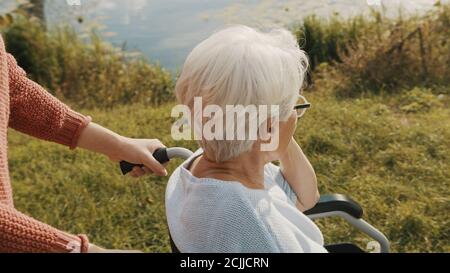 Junge Frau schiebt die alte Dame im Rollstuhl nach draußen. Überschulter-Aufnahme. Hochwertige Fotos Stockfoto
