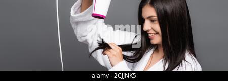 Brunette langhaarige Frau im Bademantel mit Fön isoliert auf schwarz, Panoramaaufnahme Stockfoto