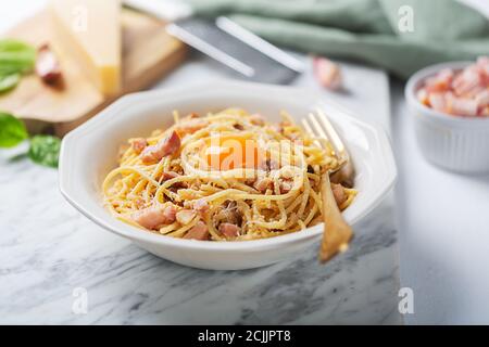 Italienische Pasta Carbonara mit Ei, Hartkäse, Schweinefleisch guanciale oder Pancetta und schwarzem Pfeffer. Gabel auf der rechten Seite der Platte Stockfoto