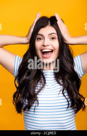 Brunette langhaarige Frau mit Locken berühren Kopf und lächeln Isoliert auf gelb Stockfoto