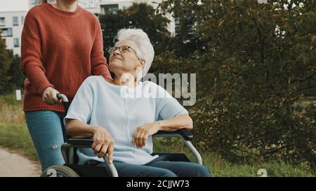 Erwachsene Enkelin, die ihrer Großmutter im Rollstuhl im Park hilft. Hochwertige Fotos Stockfoto