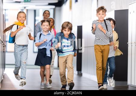 Aufgeregt multikulturelle Schüler laufen entlang Schulkorridor mit Lehrer auf Hintergrund Stockfoto