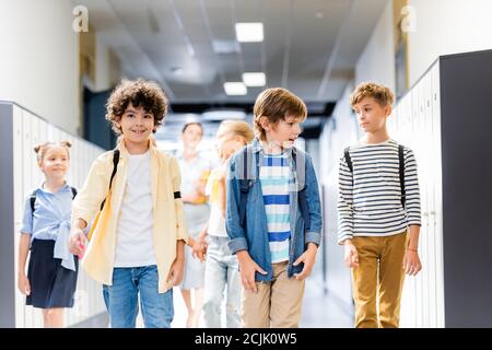 Multikulturelle Schulkinder, die auf dem Schulkorridor mit Lehrer auf dem Hintergrund spazieren Stockfoto